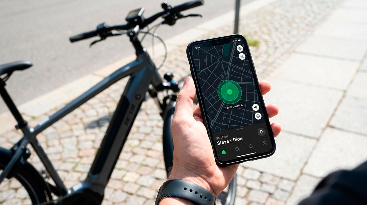 A hand holds a smartphone displaying a GPS tracking app with a detailed city map to monitor an e-bike's location in real-time