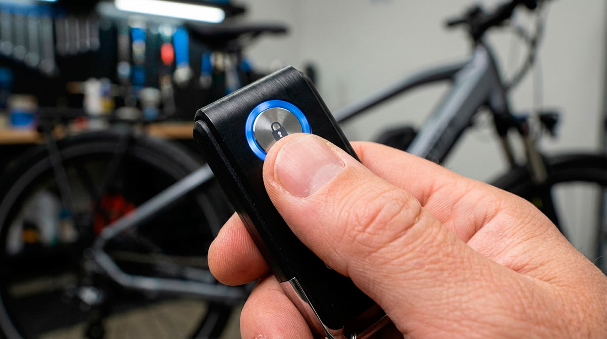 A hand pressing a button on a remote control bike alarm fob to secure an e-bike