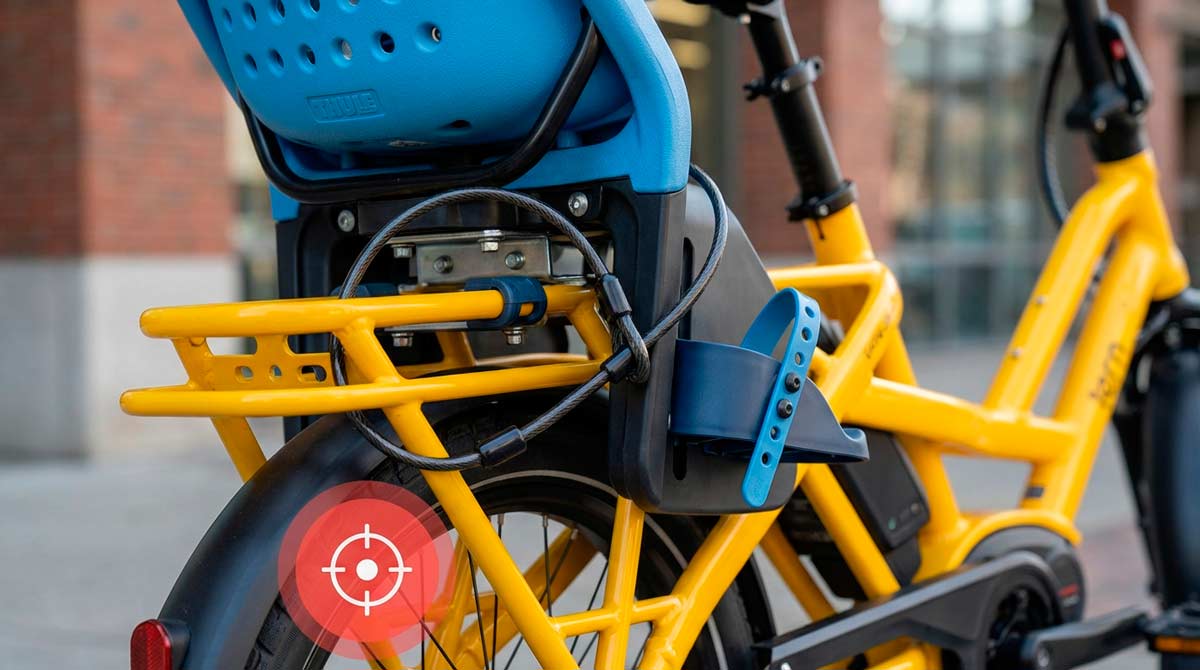 Blue Thule Yepp child seat secured with a cable lock on a yellow e-bike with a GPS tracker icon overlay